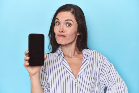 Foto de Mujer que muestra la pantalla del teléfono en el fondo azul - Imagen libre de derechos