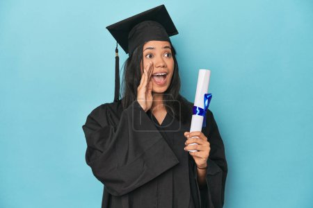 Foto de Filipina graduada con diploma en estudio azul gritando y sosteniendo la palma cerca de la boca abierta. - Imagen libre de derechos