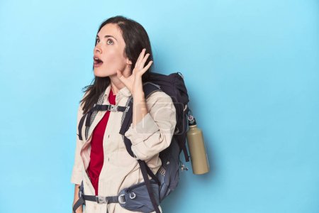Téléchargez les photos : Femme aventureuse avec sac à dos sur bleu essayant d'écouter un potins. - en image libre de droit