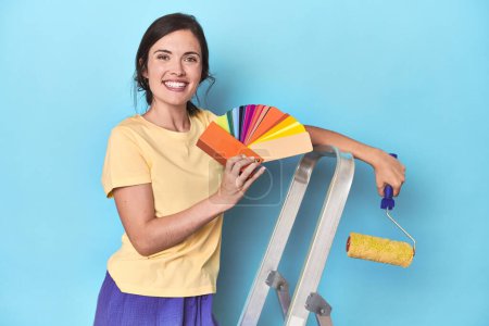 Téléchargez les photos : Femme avec palette de couleurs peinture mur sur échelle - en image libre de droit