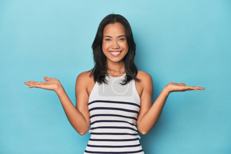 Téléchargez les photos : Philippine jeune femme sur studio bleu fait échelle avec les bras, se sent heureux et confiant. - en image libre de droit