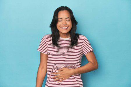 Photo for Filipina young woman on blue studio touches tummy, smiles gently, eating and satisfaction concept. - Royalty Free Image