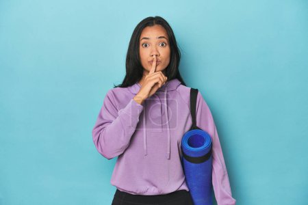 Foto de Atleta filipina con esterilla de yoga en azul guardando un secreto o pidiendo silencio. - Imagen libre de derechos