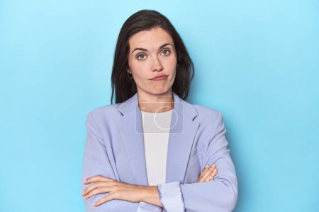 Photo for Woman in blue blazer on blue background suspicious, uncertain, examining you. - Royalty Free Image