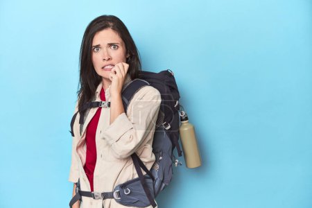 Photo for Adventurous woman with backpack on blue biting fingernails, nervous and very anxious. - Royalty Free Image