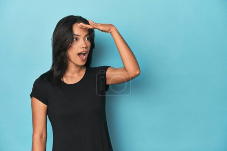 Photo for Filipina young woman on blue studio looking far away keeping hand on forehead. - Royalty Free Image