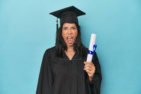 Foto de Filipina graduado con diploma en estudio azul gritando muy enojado y agresivo. - Imagen libre de derechos
