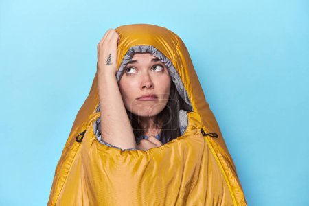Photo for Woman in sleeping bag on blue background being shocked, she has remembered important meeting. - Royalty Free Image