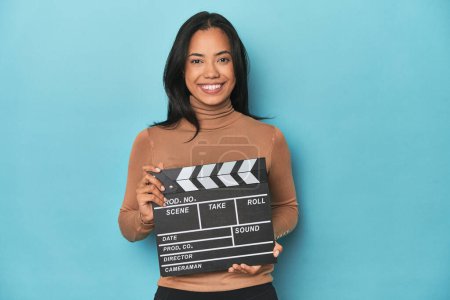 Téléchargez les photos : Filipina avec film clapperboard sur fond bleu studio - en image libre de droit