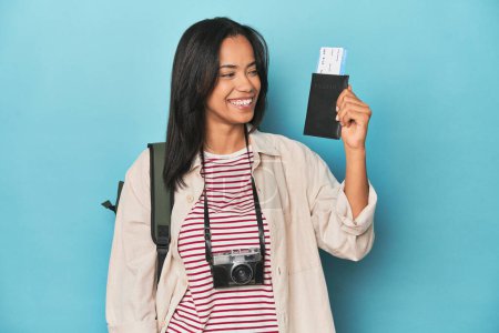 Photo for Filipina traveler displaying flight ticket with camera and backpack on blue - Royalty Free Image