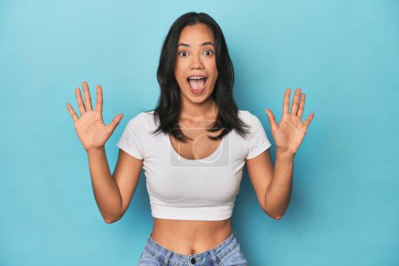 Photo for Filipina young woman on blue studio receiving a pleasant surprise, excited and raising hands. - Royalty Free Image