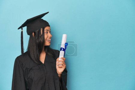 Téléchargez les photos : Célébration Filipina diplômé avec diplôme et casquette sur studio bleu - en image libre de droit