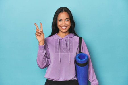 Photo for Filipina athlete with yoga mat on blue showing number two with fingers. - Royalty Free Image