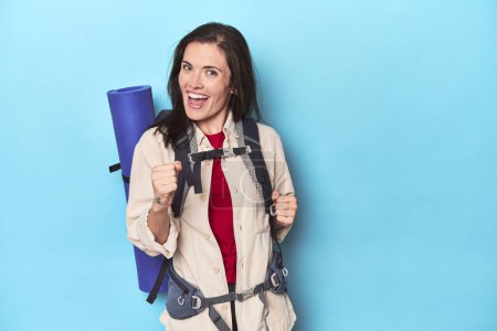 Téléchargez les photos : Femme aventureuse avec sac à dos et tapis sur bleu - en image libre de droit