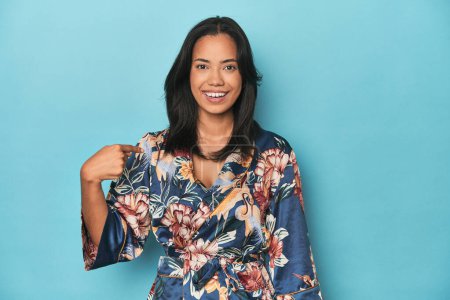 Photo for Filipina in floral kimono on blue studio person pointing by hand to a shirt copy space, proud and confident - Royalty Free Image