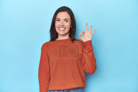Photo for Young caucasian woman on blue backdrop cheerful and confident showing ok gesture. - Royalty Free Image