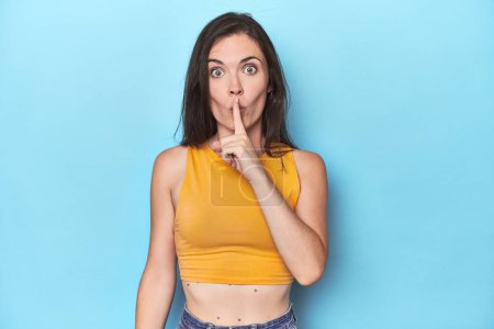 Photo for Young caucasian woman on blue backdrop keeping a secret or asking for silence. - Royalty Free Image