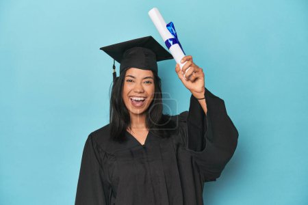 Foto de Celebrando Filipina graduado con diploma y gorra en estudio azul - Imagen libre de derechos