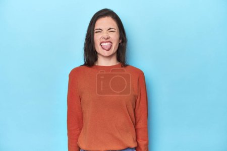 Foto de Joven mujer caucásica en azul telón de fondo divertido y amigable sobresaliendo lengua. - Imagen libre de derechos