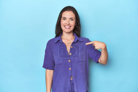 Photo for Young caucasian woman on blue backdrop person pointing by hand to a shirt copy space, proud and confident - Royalty Free Image