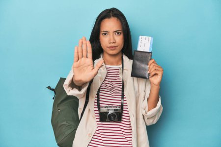 Téléchargez les photos : Filipina avec caméra, billets, sac à dos sur pied bleu avec la main tendue montrant le panneau stop, vous empêchant. - en image libre de droit