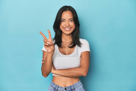 Photo for Filipina young woman on blue studio showing number two with fingers. - Royalty Free Image