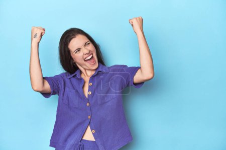 Foto de Joven mujer caucásica sobre fondo azul levantando puño después de una victoria, concepto ganador. - Imagen libre de derechos