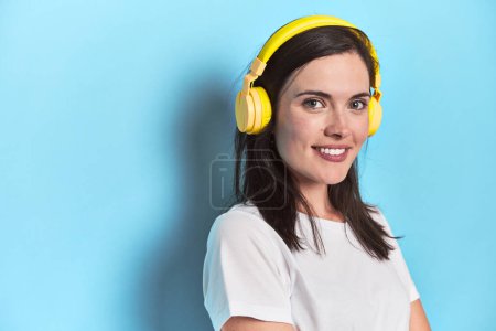 Téléchargez les photos : Jeune femme immergée dans la musique avec écouteurs sur bleu - en image libre de droit