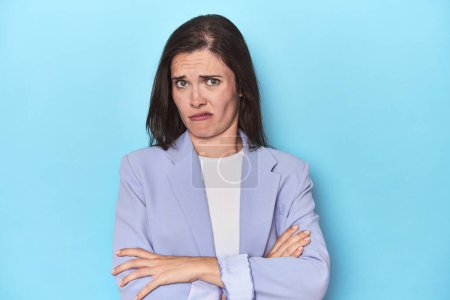 Photo for Woman in blue blazer on blue background unhappy looking in camera with sarcastic expression. - Royalty Free Image