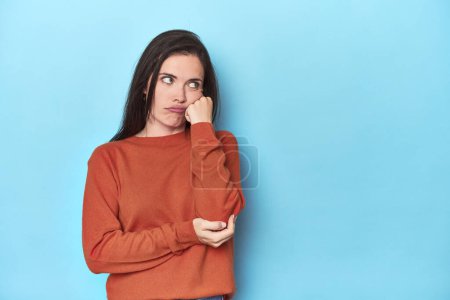 Photo for Young caucasian woman on blue backdrop who feels sad and pensive, looking at copy space. - Royalty Free Image