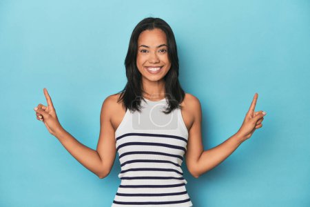Téléchargez les photos : Philippine jeune femme sur studio bleu indique avec les deux doigts avant montrant un espace vide. - en image libre de droit