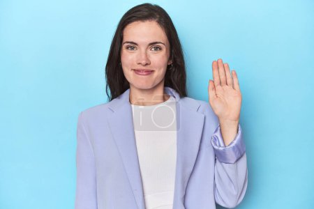 Photo for Woman in blue blazer on blue background smiling cheerful showing number five with fingers. - Royalty Free Image