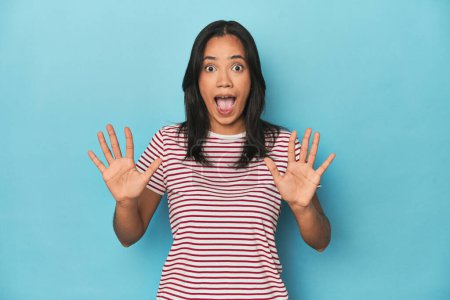 Téléchargez les photos : Philippine jeune femme sur studio bleu recevant une agréable surprise, excité et levant la main. - en image libre de droit