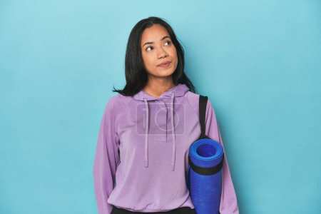 Photo for Filipina athlete with yoga mat on blue dreaming of achieving goals and purposes - Royalty Free Image