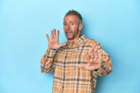 Photo for Middle-aged caucasian man on blue backdrop being shocked due to an imminent danger - Royalty Free Image