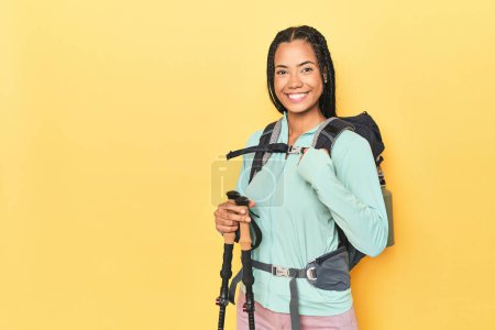 Téléchargez les photos : Femme indonésienne avec équipement de randonnée sur la personne jaune pointant à la main vers un espace de copie de chemise, fière et confiante - en image libre de droit