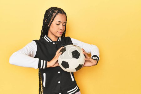 Photo for Young Indonesian woman with medal and soccer ball on yellow studio background - Royalty Free Image