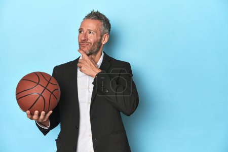 Photo for Middle-aged basketball coach on blue backdrop Middle-aged basketball coach on blue backdroplooking sideways with doubtful and skeptical expression. - Royalty Free Image