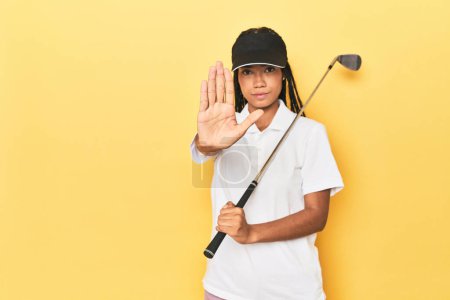 Téléchargez les photos : Golfeuse indonésienne sur fond jaune debout avec la main tendue montrant le signe d'arrêt, vous empêchant. - en image libre de droit