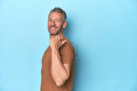 Foto de Hombre caucásico de mediana edad en puntos de fondo azules con el dedo pulgar lejos, riendo y sin preocupaciones. - Imagen libre de derechos