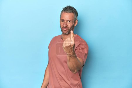 Photo for Middle-aged caucasian man on blue backdrop pointing with finger at you as if inviting come closer. - Royalty Free Image