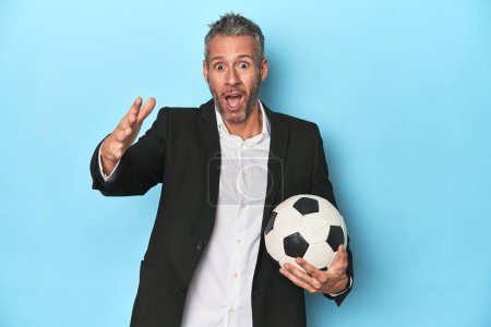 Photo for Caucasian football coach, middle-aged on blue set receiving a pleasant surprise, excited and raising hands. - Royalty Free Image