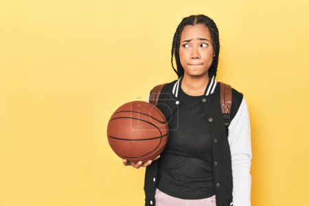 Photo for Indonesian schoolgirl with basketball on yellow confused, feels doubtful and unsure. - Royalty Free Image