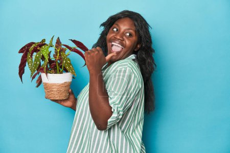 Foto de Curvy jardinero sosteniendo la planta en puntos de estudio con el dedo pulgar lejos, riendo y sin preocupaciones. - Imagen libre de derechos