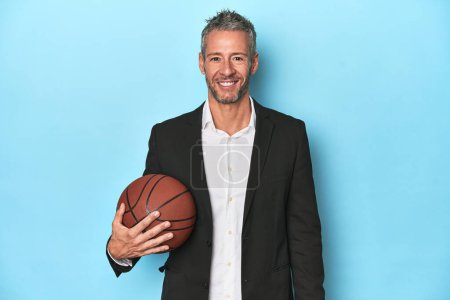 Photo for Basketball coach holding a ball on blue studio backdrop - Royalty Free Image