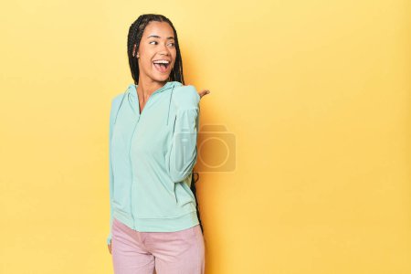 Foto de Mujer deportiva indonesia en puntos de fondo amarillos con el dedo pulgar lejos, riendo y sin preocupaciones. - Imagen libre de derechos