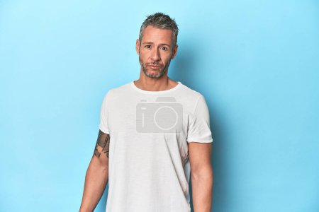 Téléchargez les photos : Homme d'âge moyen posant sur fond de studio bleu - en image libre de droit
