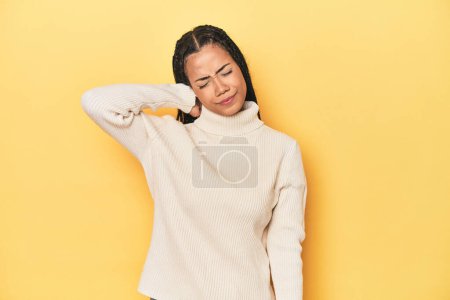 Photo for Young Indonesian woman on yellow studio backdrop suffering neck pain due to sedentary lifestyle. - Royalty Free Image