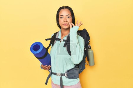 Photo for Indonesian woman ready for mountain trip on yellow with fingers on lips keeping a secret. - Royalty Free Image