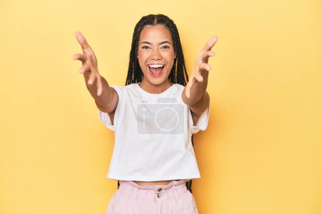 Photo for Young Indonesian woman on yellow studio backdrop feels confident giving a hug to the camera. - Royalty Free Image